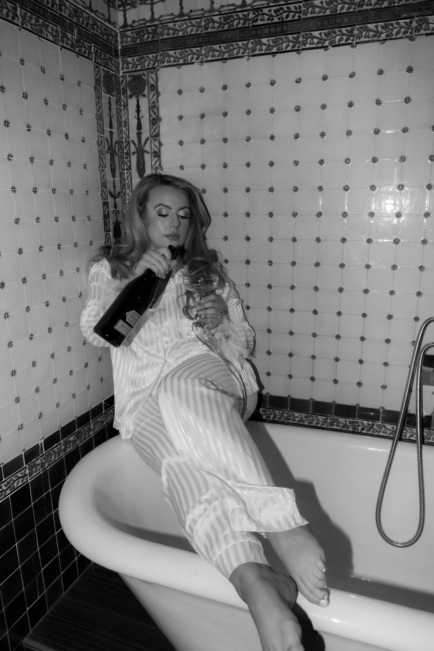 bride pouring champagne into glass on the side of the bath during bridal prep photos