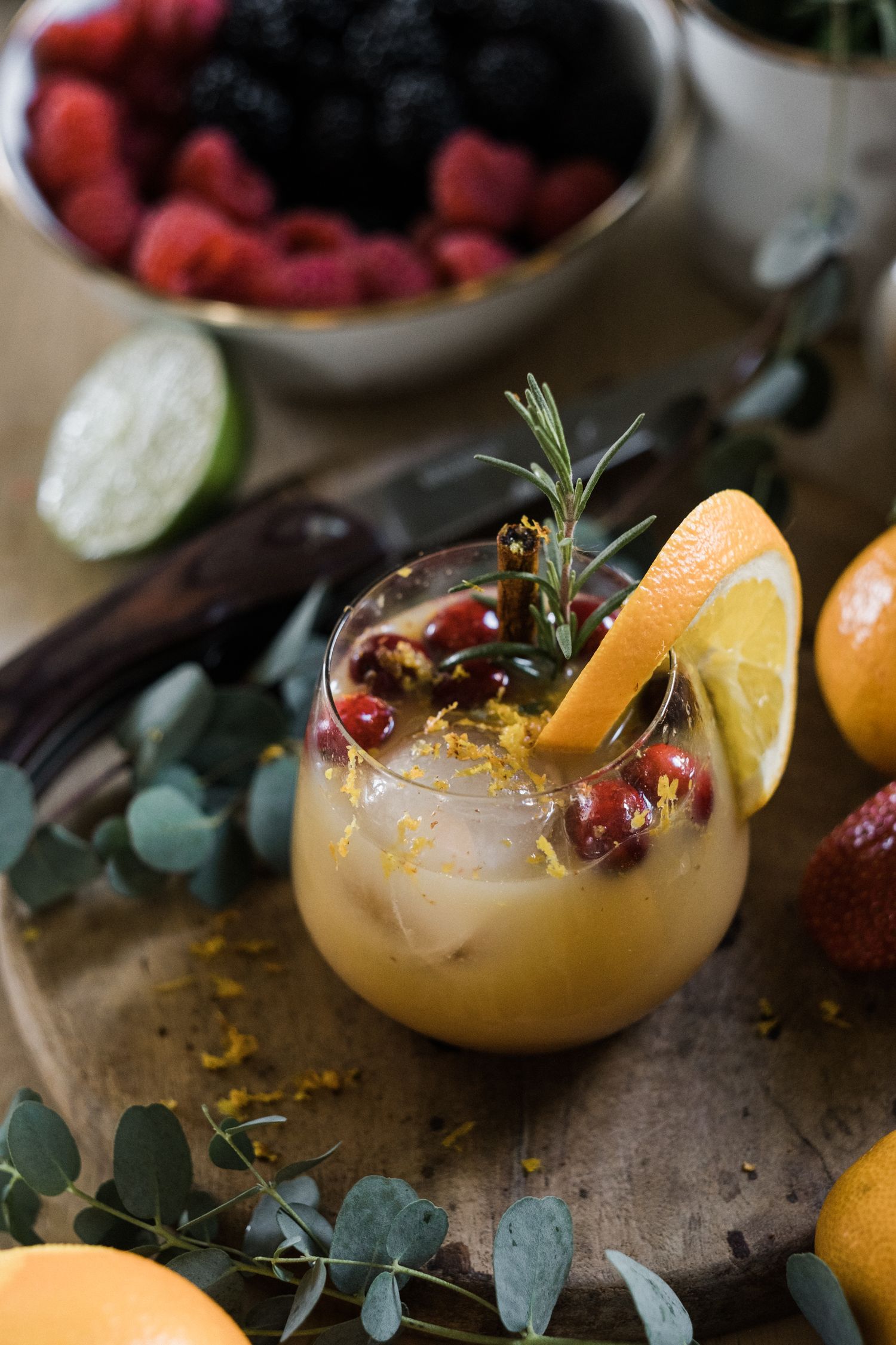 Citrus cocktail garnished with pomegranate seeds and herbs on a rustic surface.