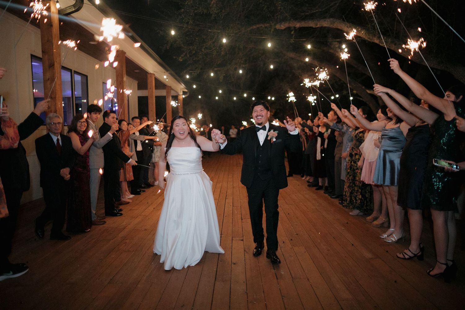 Wedding couple exits reception through sparkler tunnel lined with guests.
