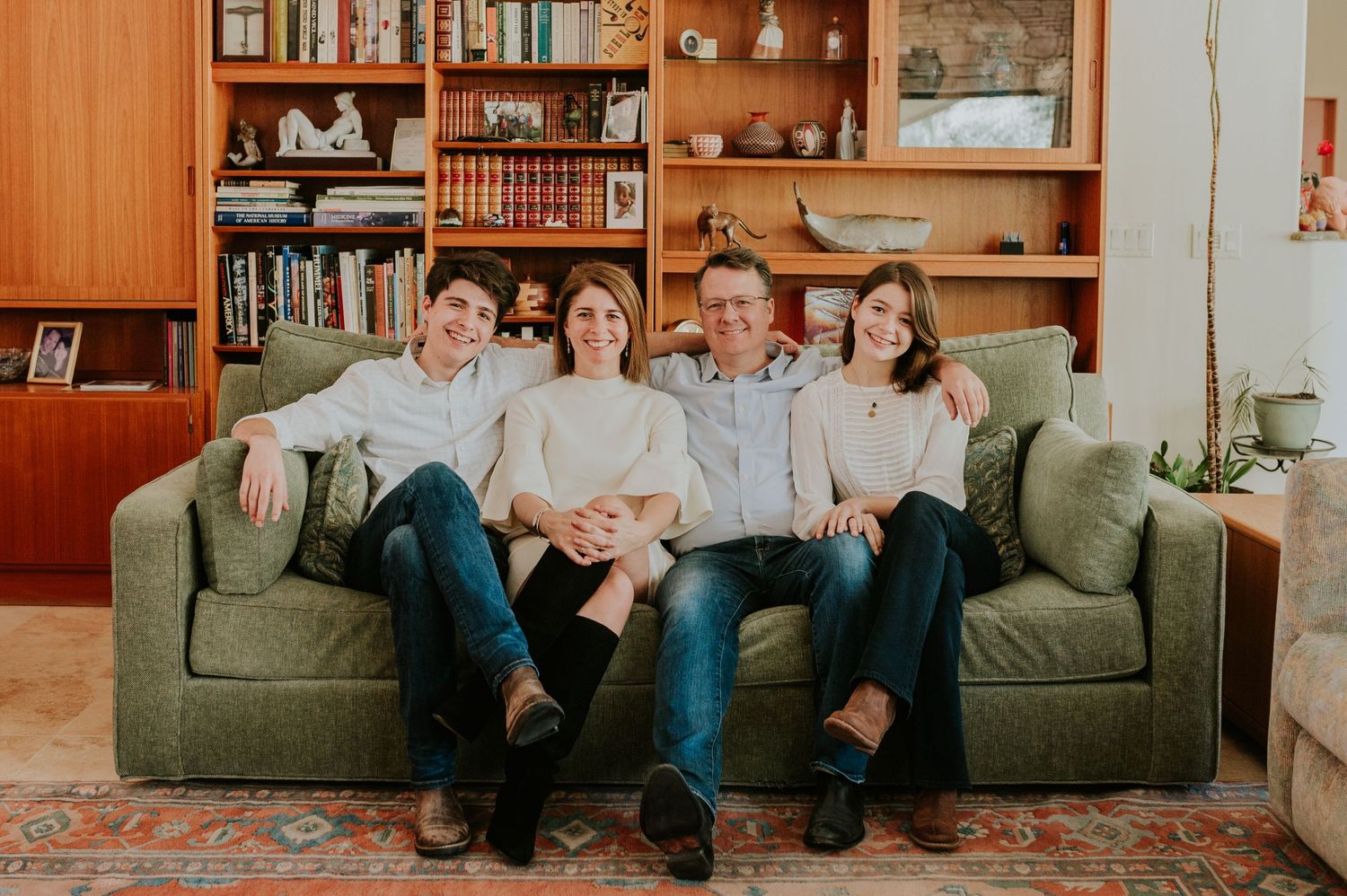 Family group relaxing together on a gray couch in front of wooden bookshelves.