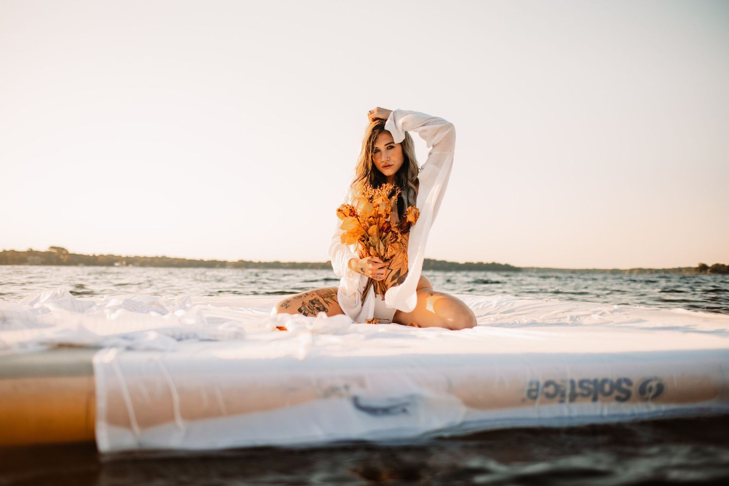 Woman in white sitting on surfboard at beach during golden hour.