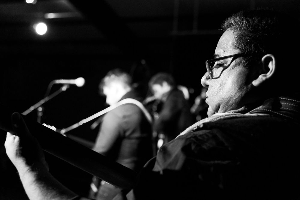 A musician performs in black and white lighting while playing guitar at a small venue.