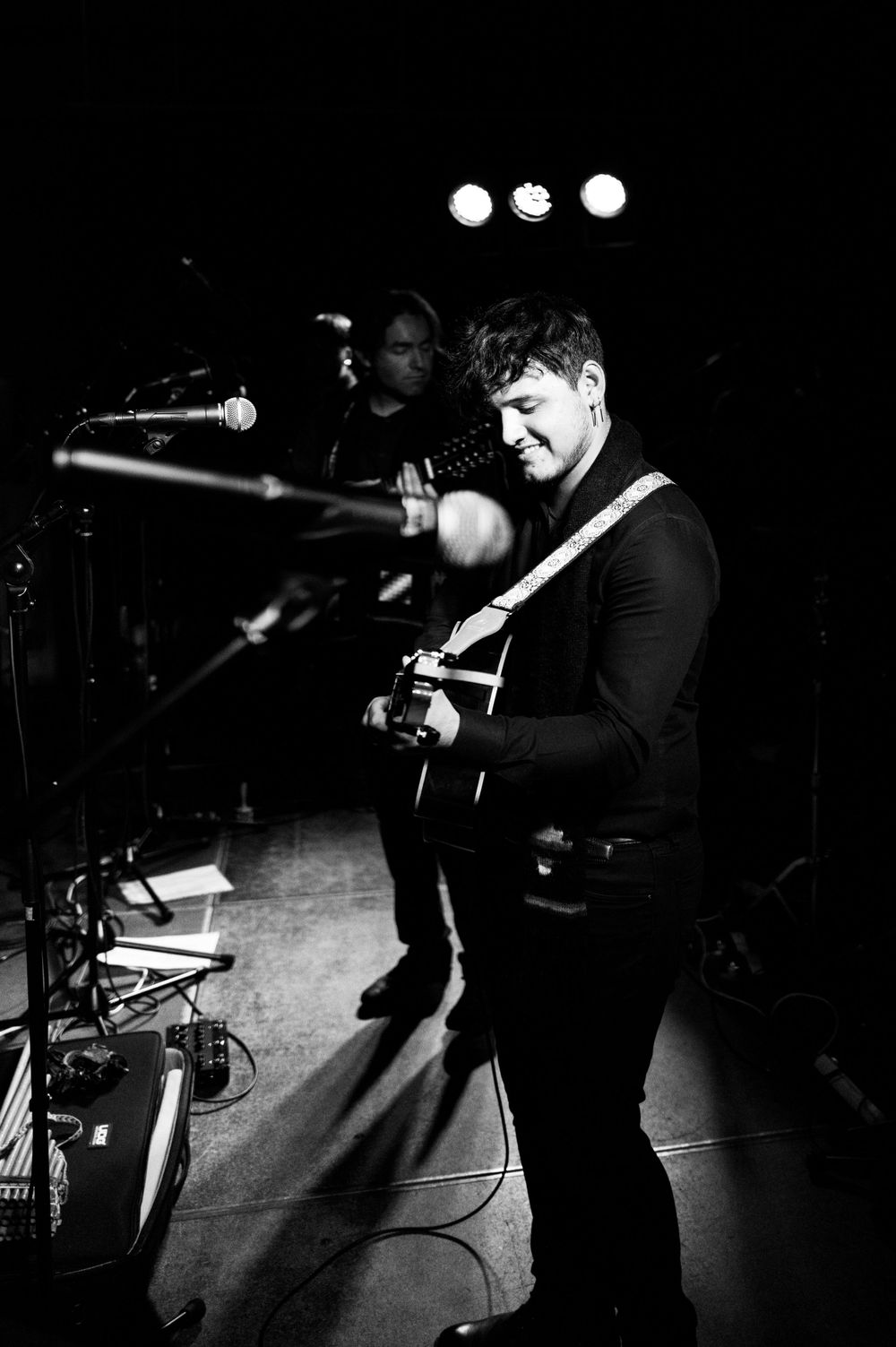 A guitarist performs in dramatic black and white lighting during an intimate concert.
