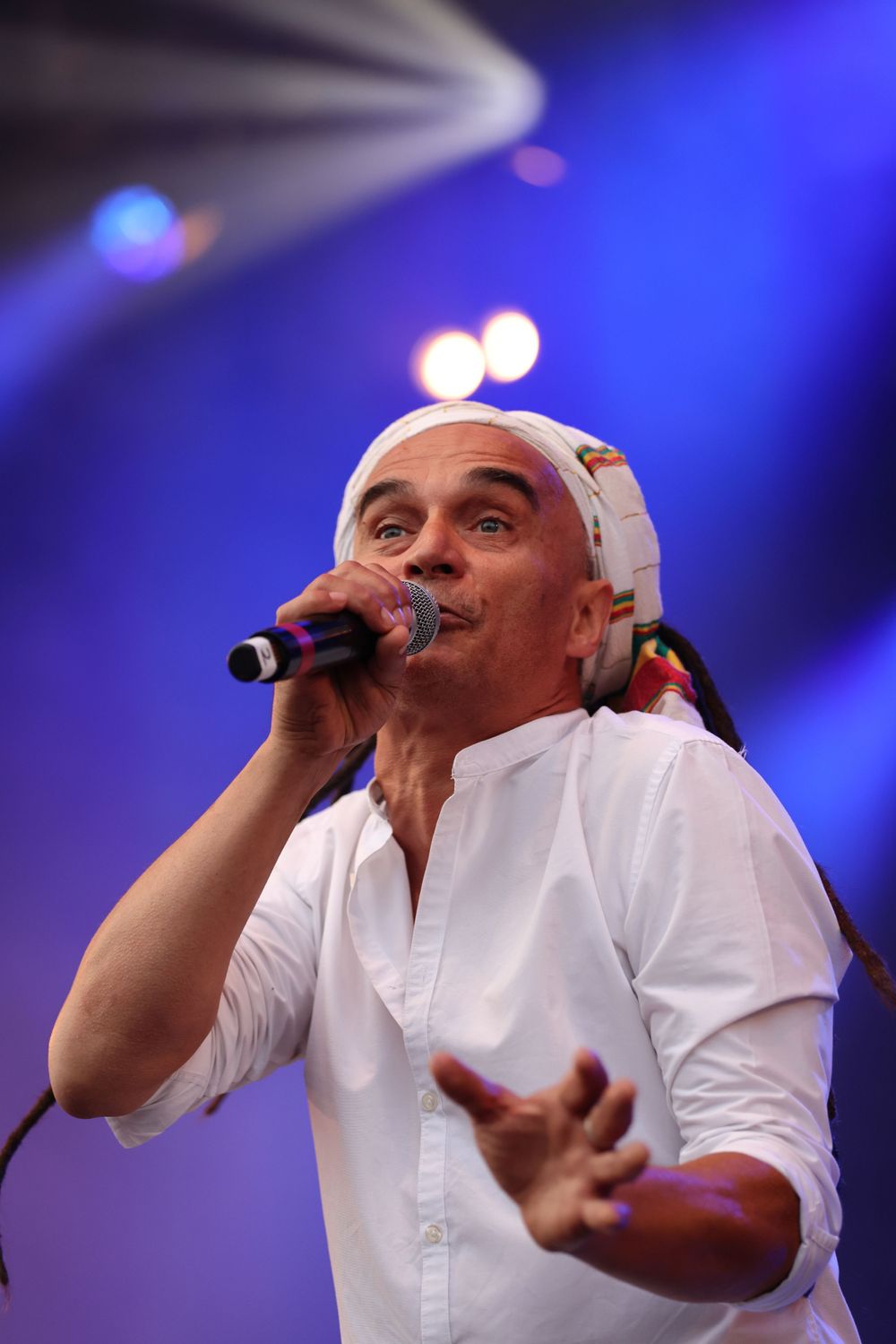 Performer in white shirt sings passionately into microphone under blue stage lights.