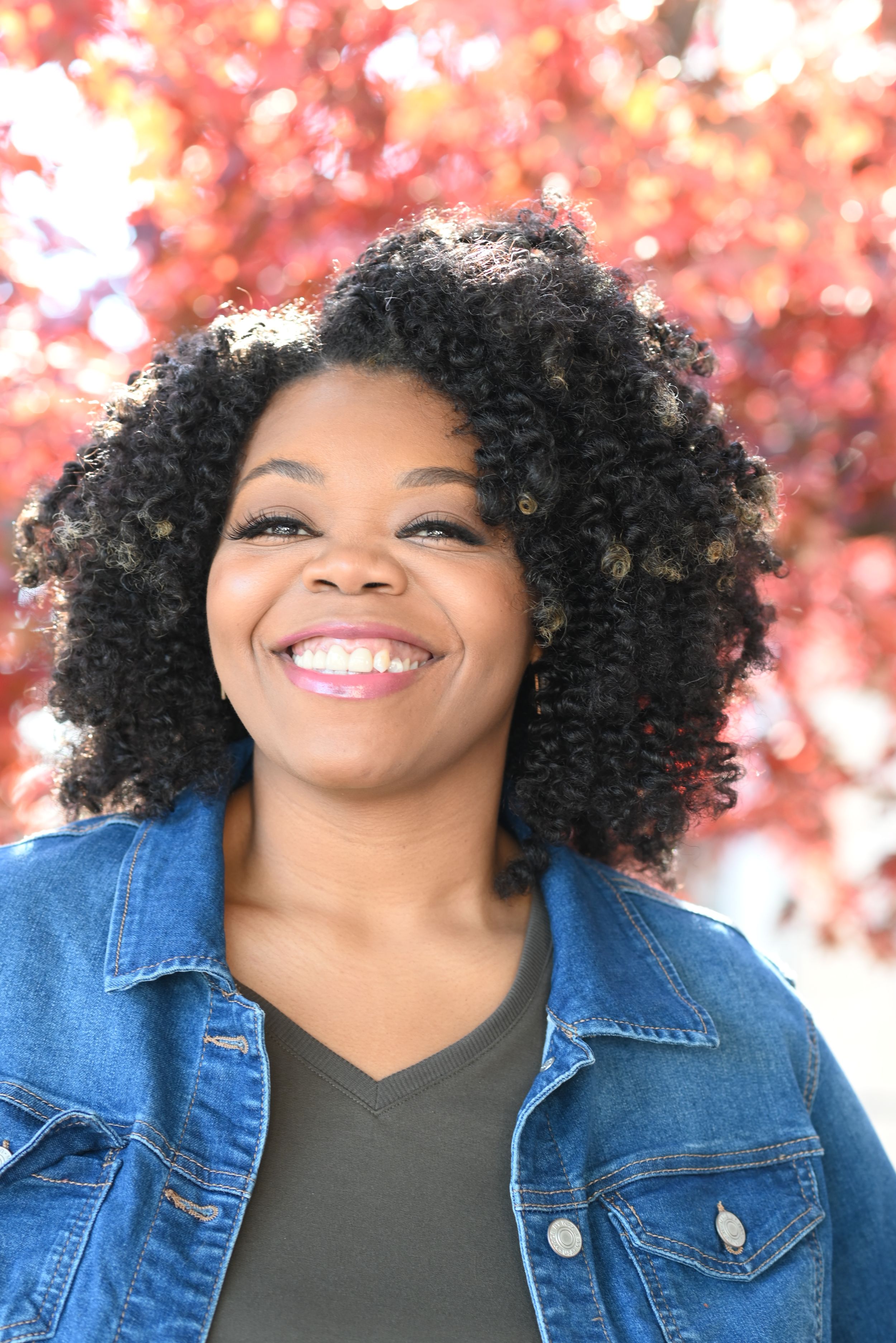 Pixs By Tina captures actress Kala William in a denim jacket and curly hair smiling against a pink autumn background.