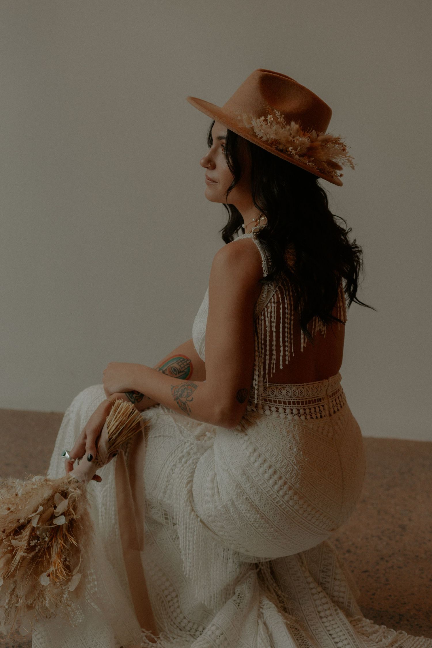 Artistic side view of a bride in a detailed lace gown wearing a brown hat with feather accents.