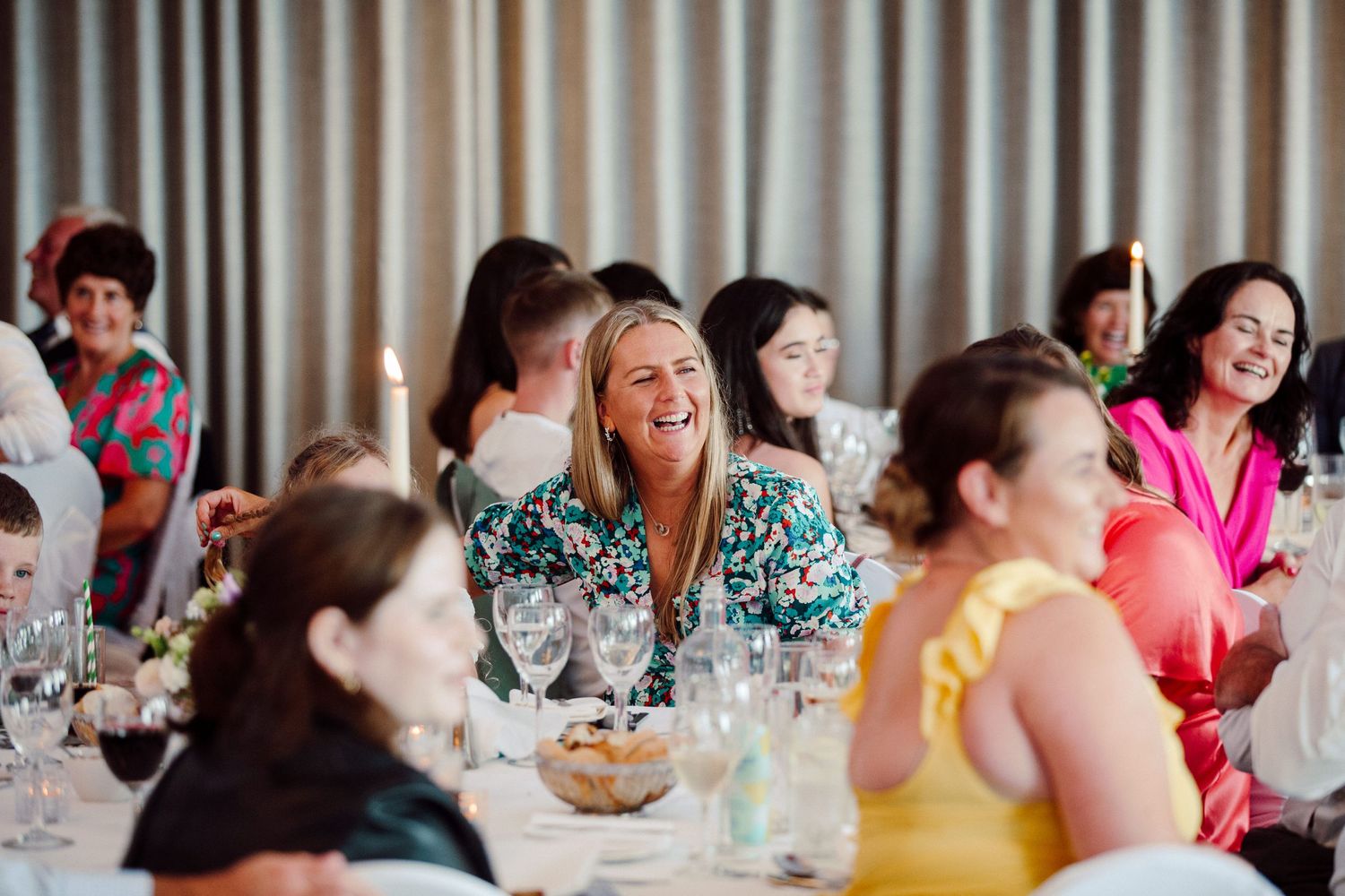 Wedding guests laugh and smile during a reception dinner at decorated tables.