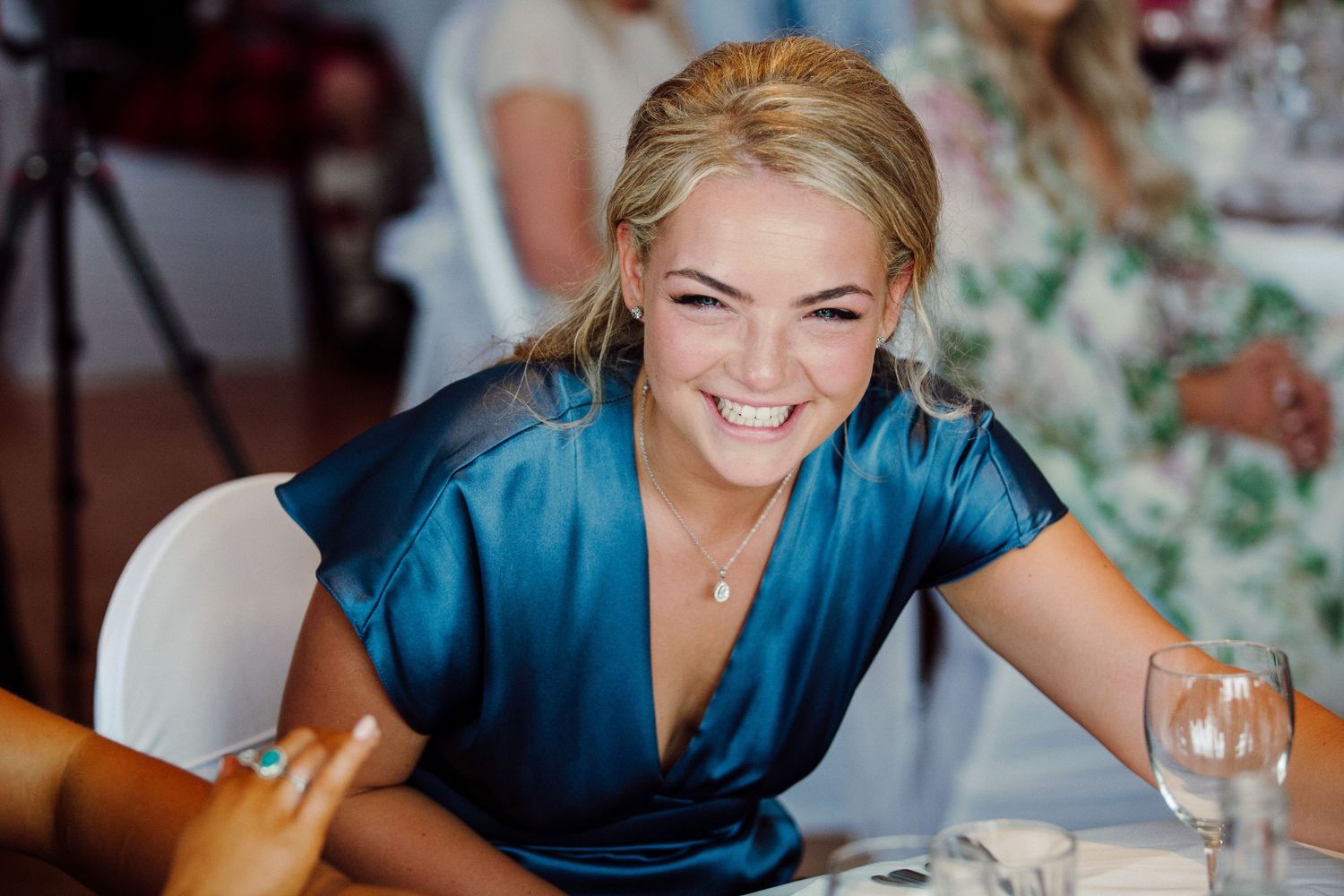 Guest in blue dress laughs joyfully during wedding reception.