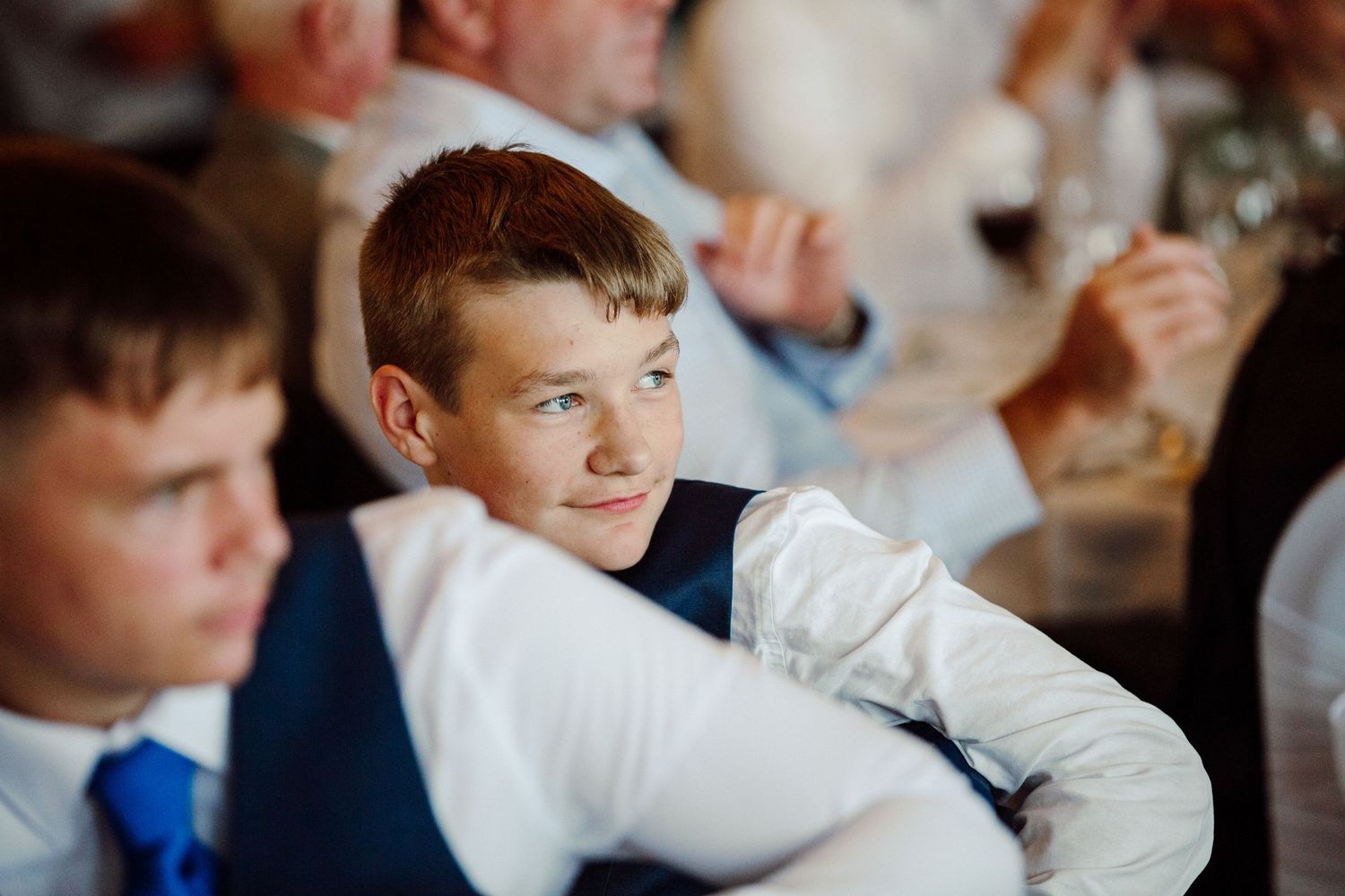 Young guest in formal attire smiles during wedding reception.