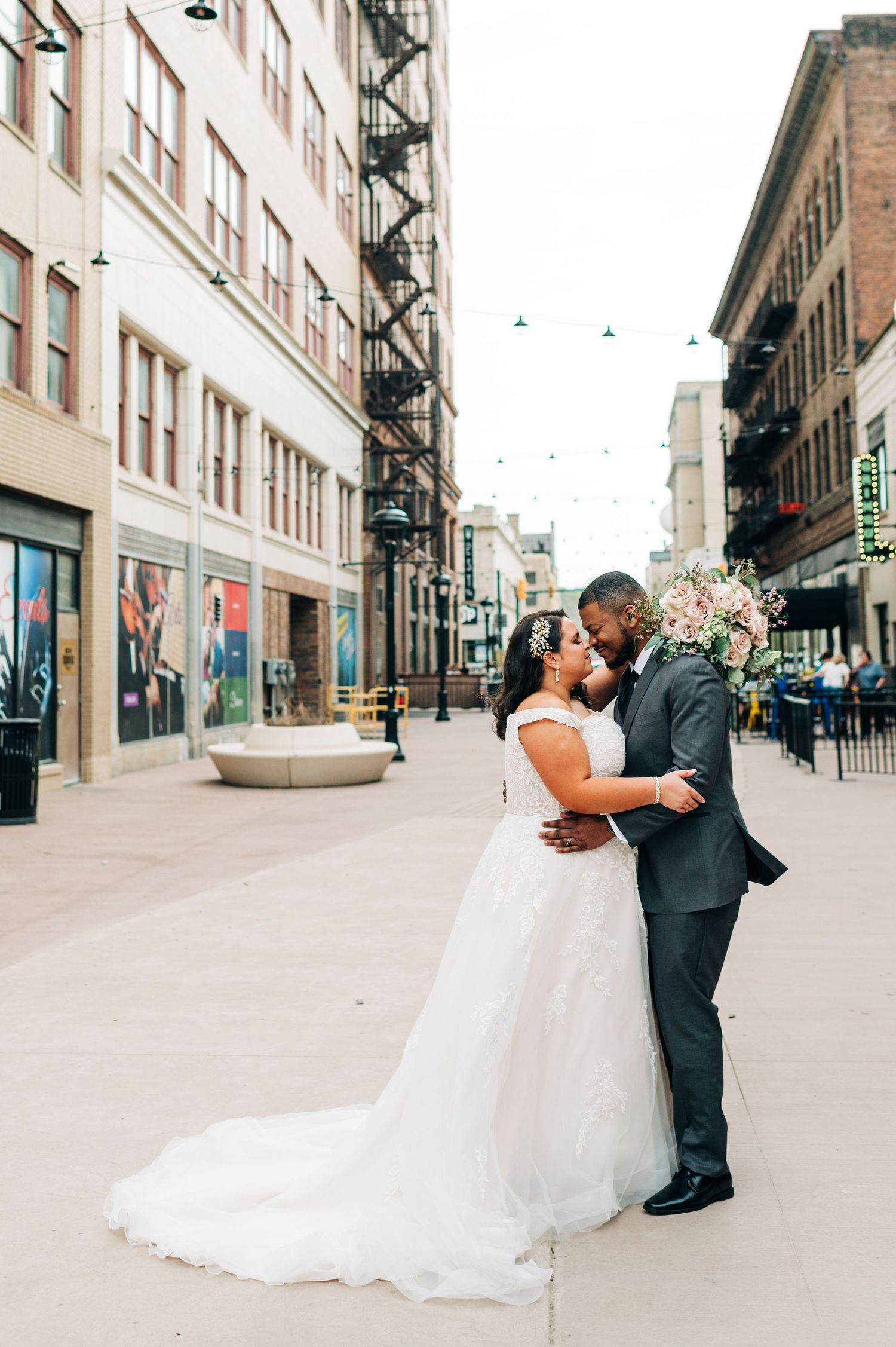 Wedding couple sharing an intimate moment on an urban street with brick buildings and a decorative planter.