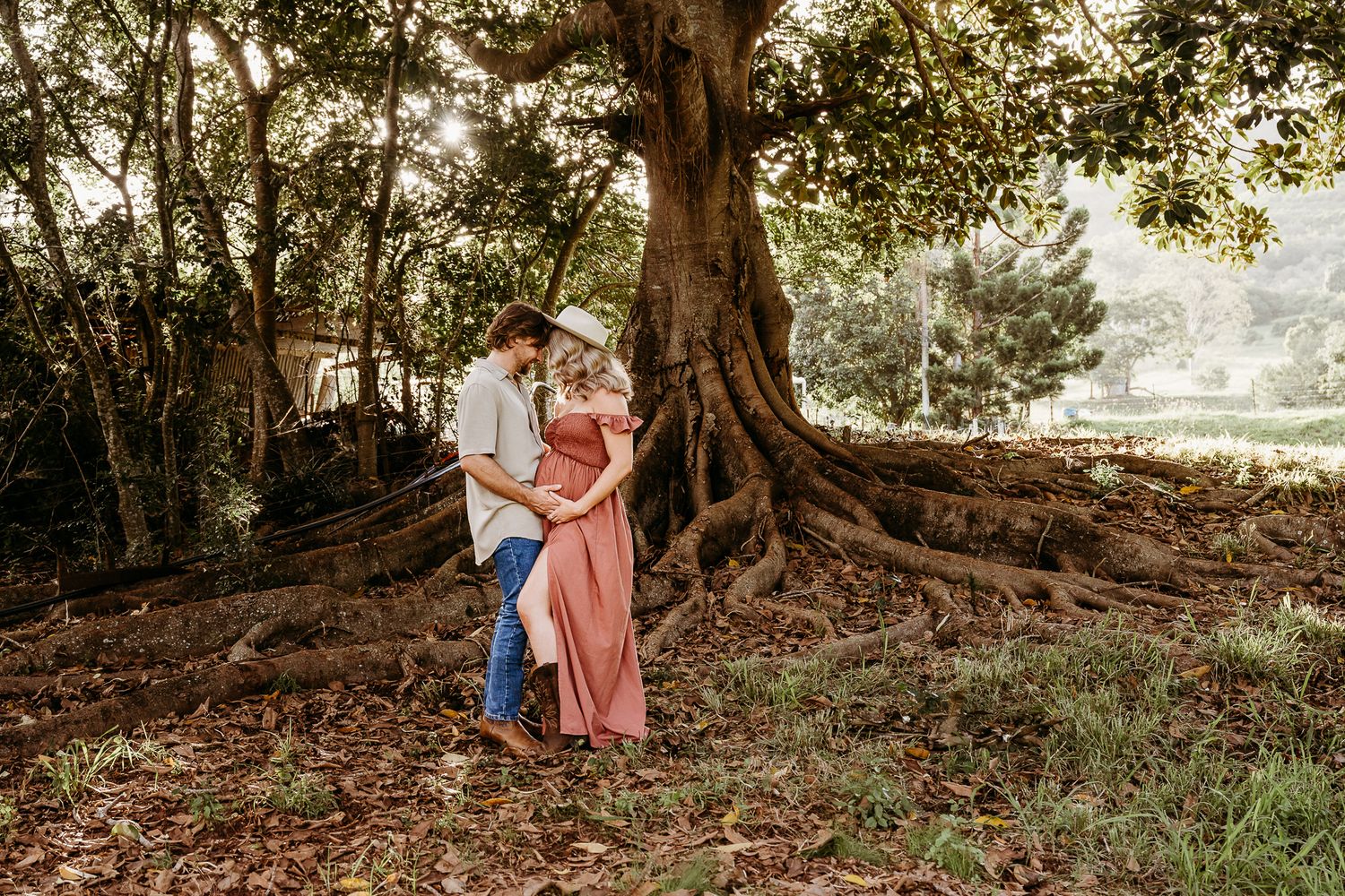 A couple embraces beneath a massive tree with exposed roots in a romantic outdoor photo shoot.