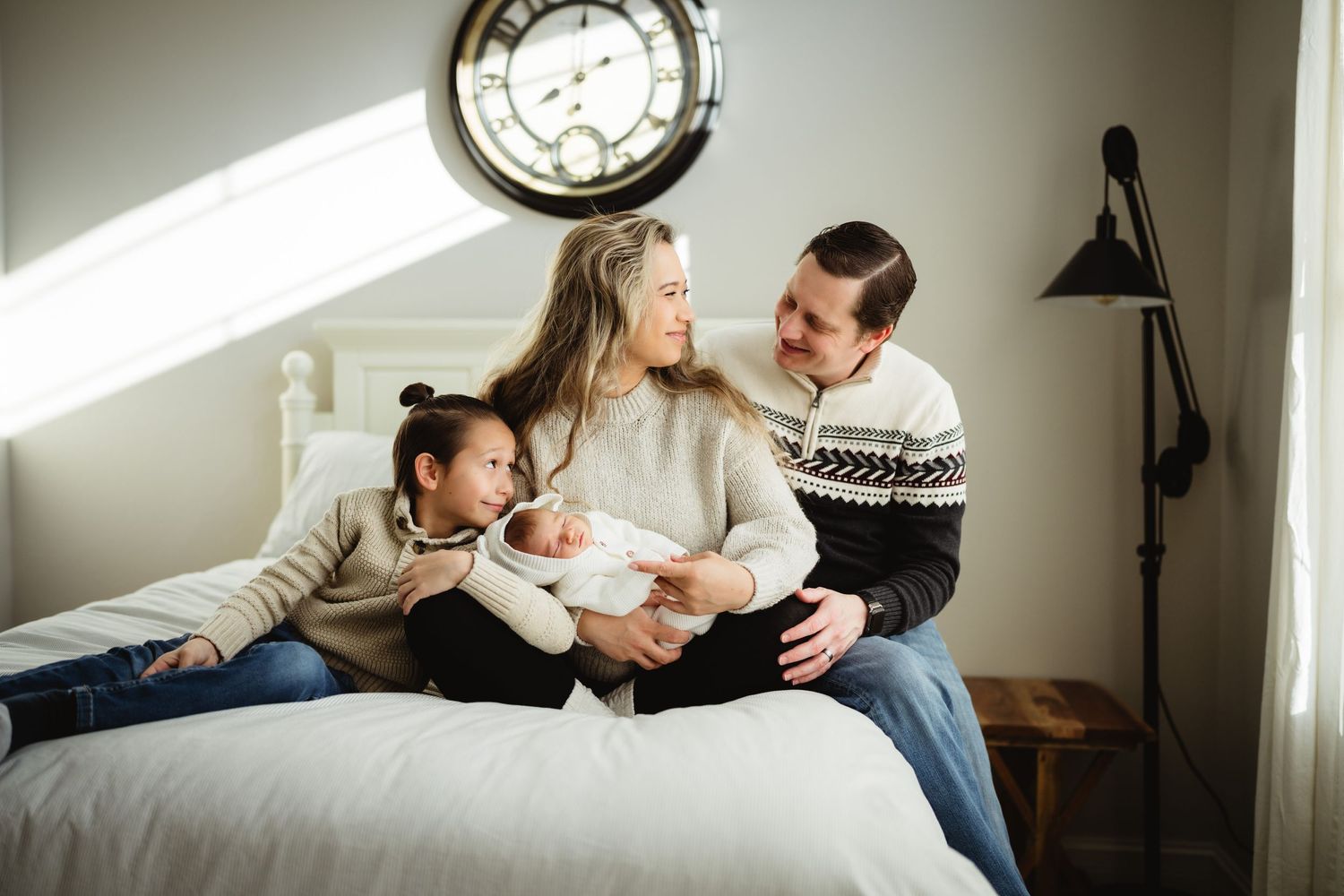 A family shares a joyful moment together on a bed under a wall clock.