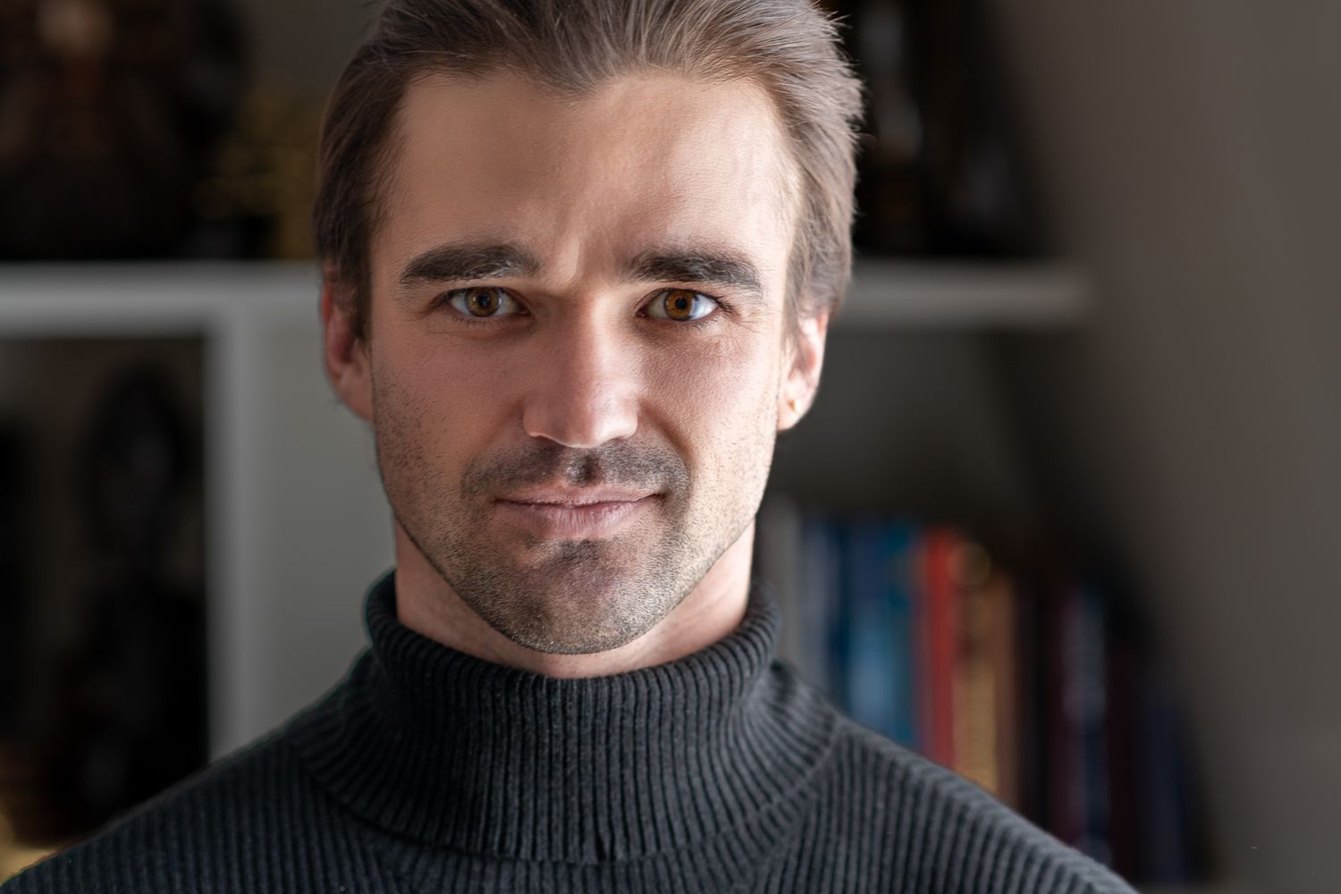 a young man in a black turtleneck stands in front of a bookcase in Paris