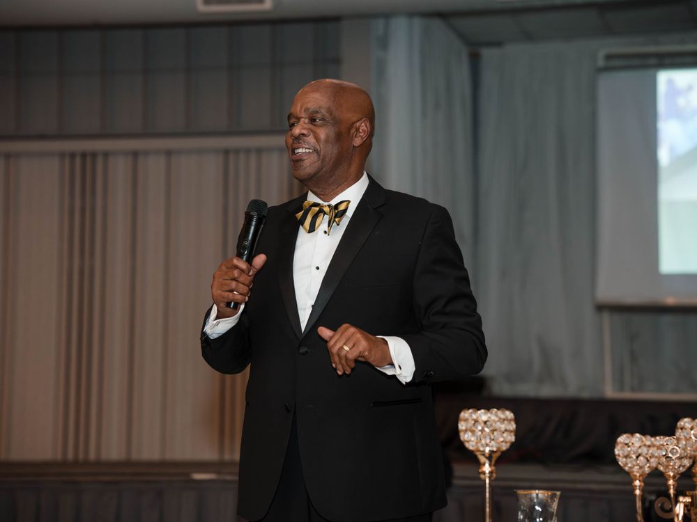 Speaker in formal black tuxedo and bow tie giving a speech at an elegant event.
