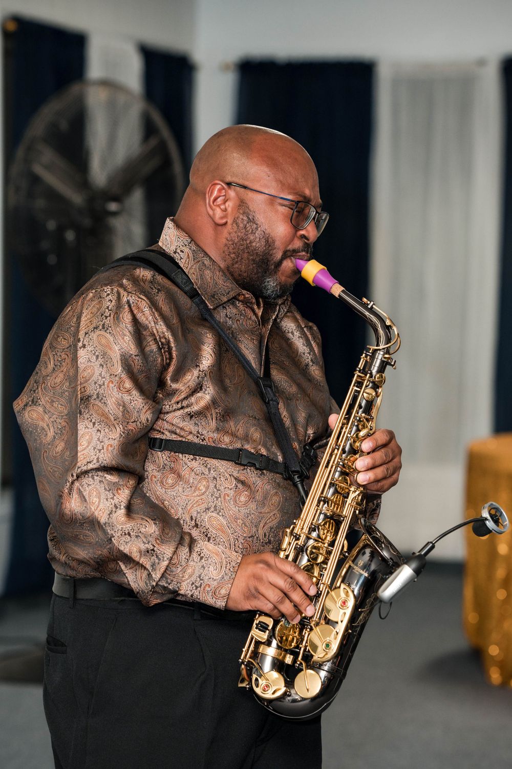 Saxophone player performing in an elegant bronze patterned shirt on stage.