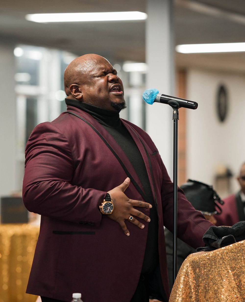 Performer singing passionately into microphone while wearing burgundy blazer at formal event.