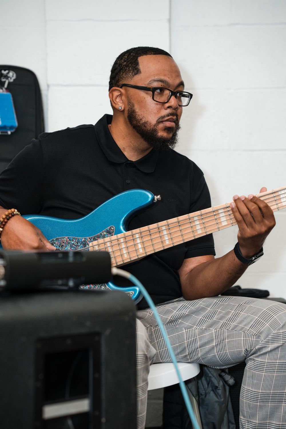 Musician playing a bright blue electric bass guitar while wearing glasses and a black shirt.