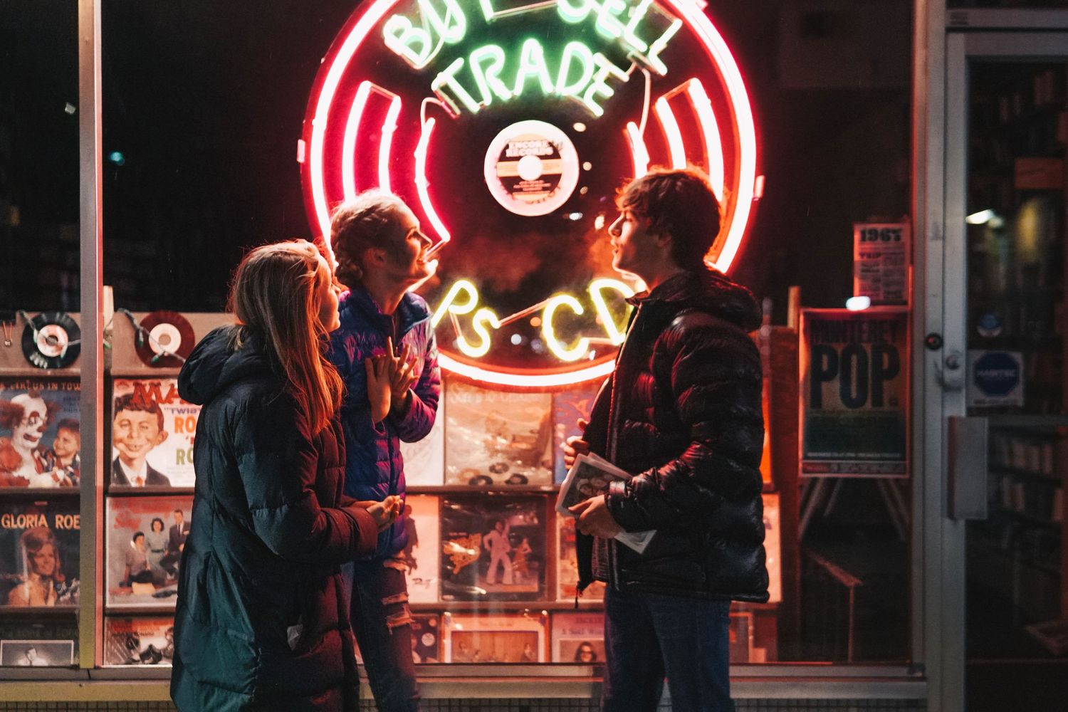 People silhouetted against colorful neon signs at night outside a business.