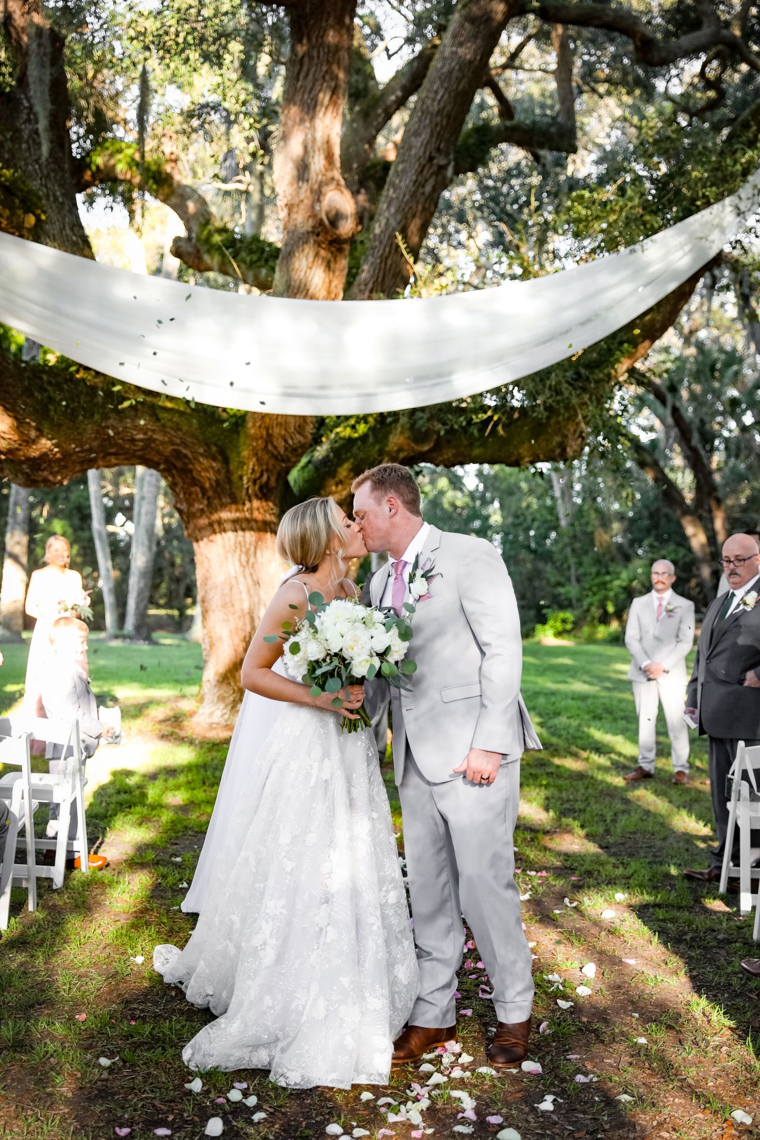 Romantic outdoor wedding ceremony moment under moss-draped oak trees.
