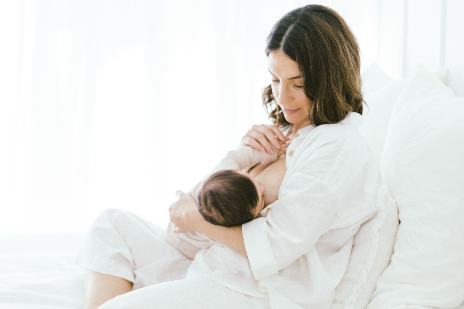 Serene nursing moment captured in soft white tones against light background.