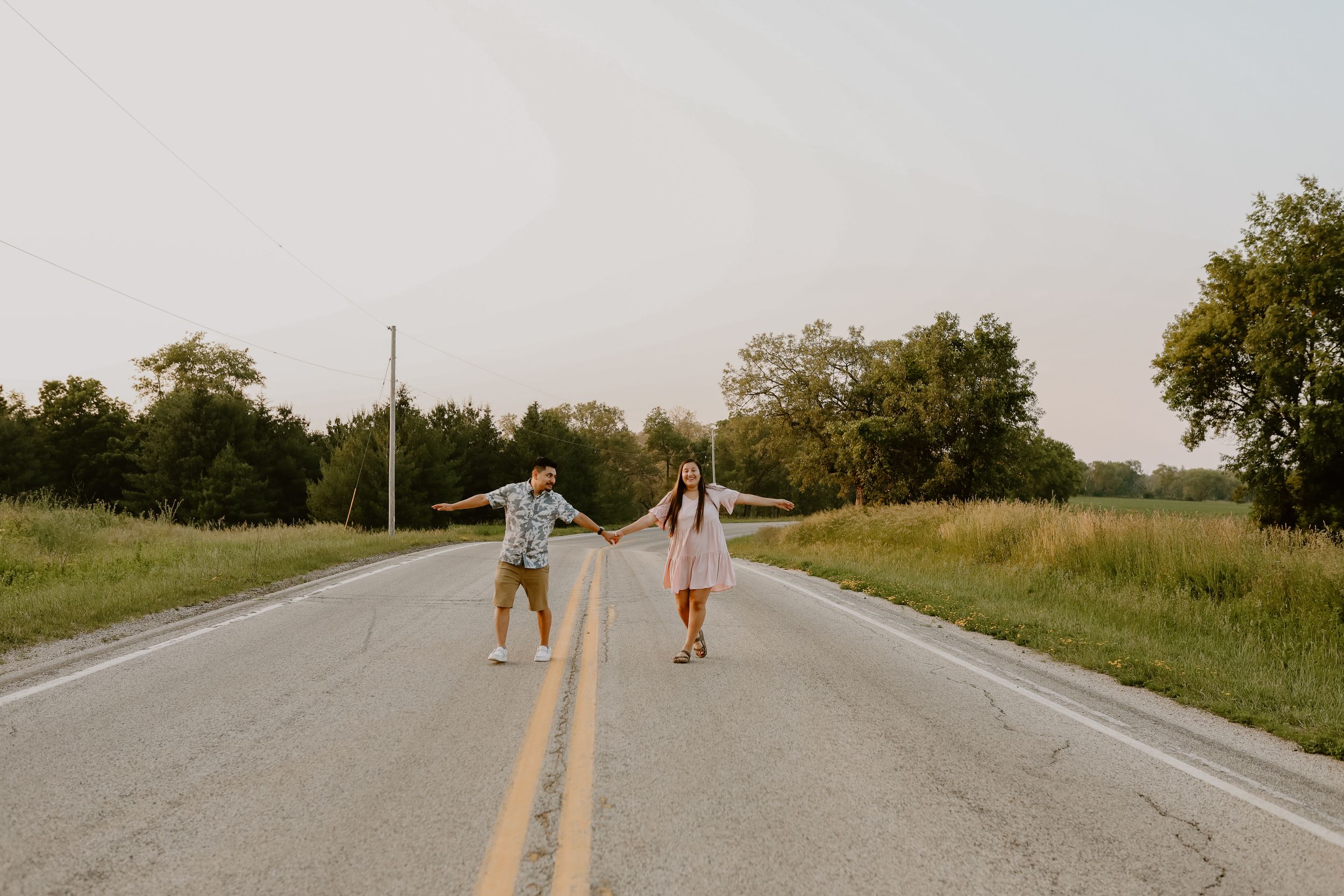 Two people hold hands while walking down middle of empty rural road at sunset.