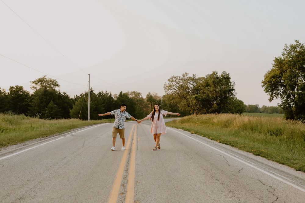 Two people hold hands while walking down middle of empty rural road at sunset.
