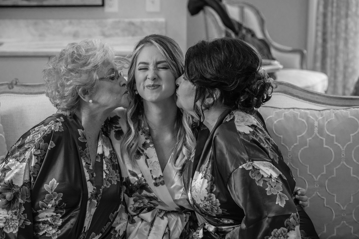 Black and white candid moment showing three people sharing laughter on a sofa.