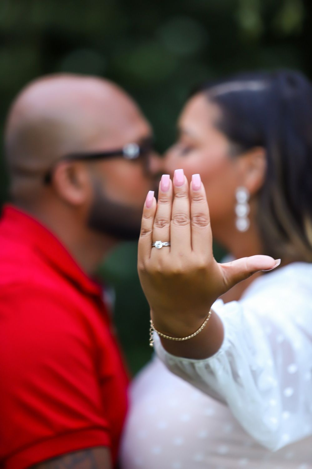 Close up of engagement ring with couple embracing in background.