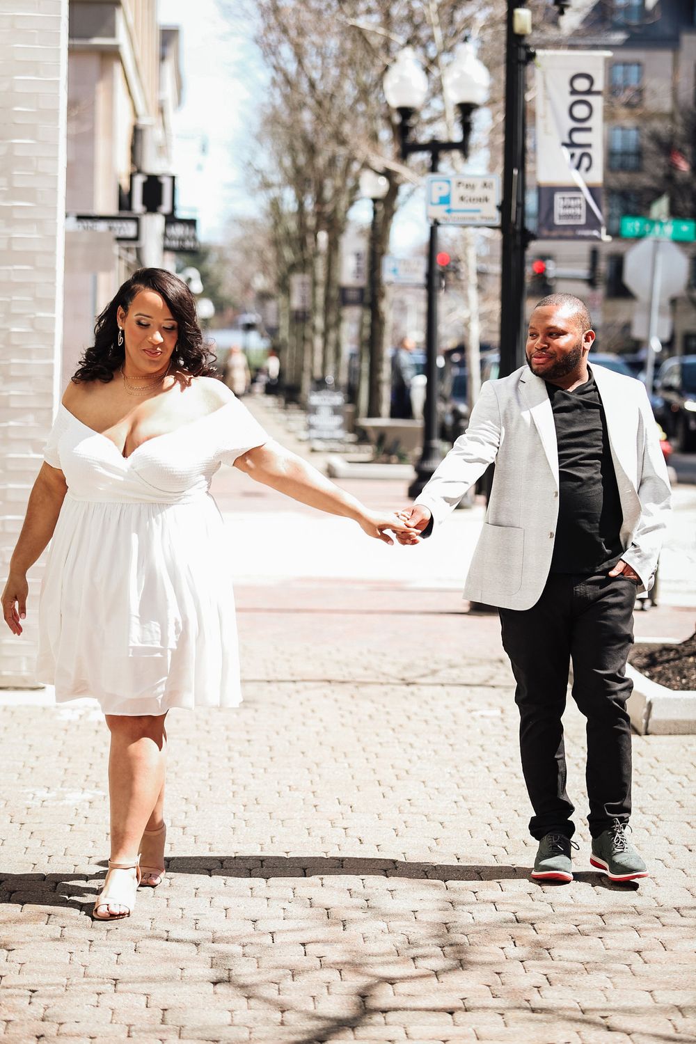 Couple in formal white and black attire walking hand in hand on city street.