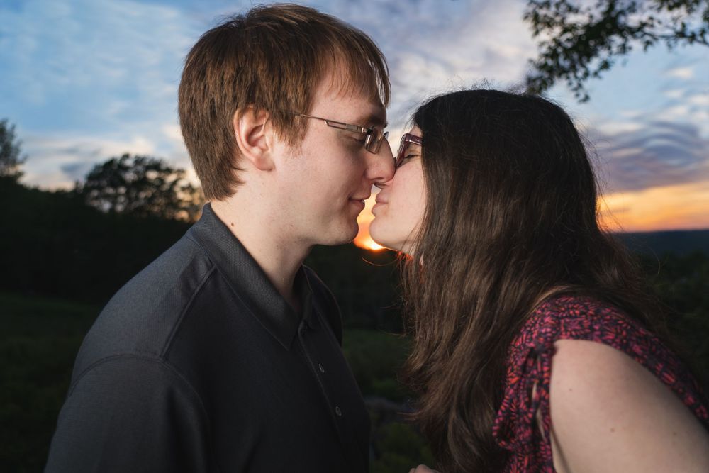 Two people share an intimate moment against a bright blue sky and clouds.
