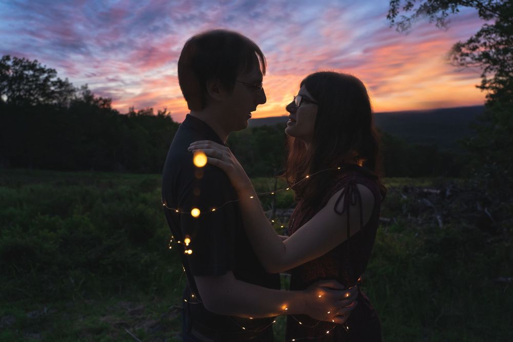 A couple silhouetted against a dramatic purple and orange sunset sky with string lights.