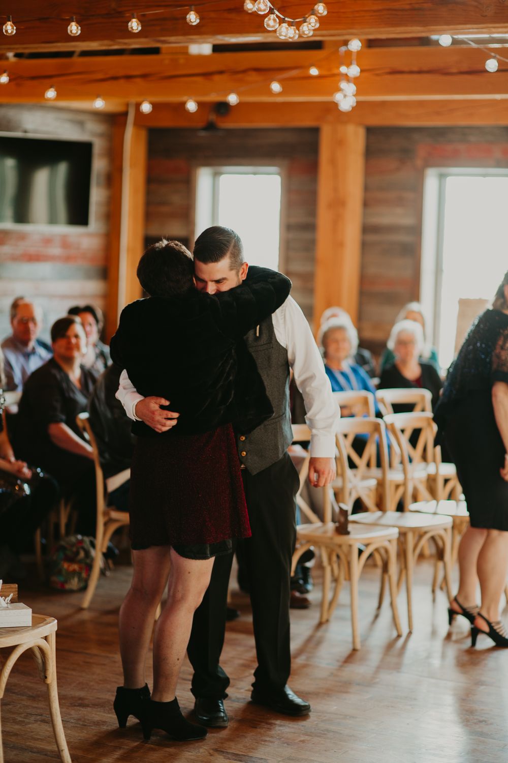 Groom shares a heartfelt hug with a guest during a rustic barn wedding reception with string lights.