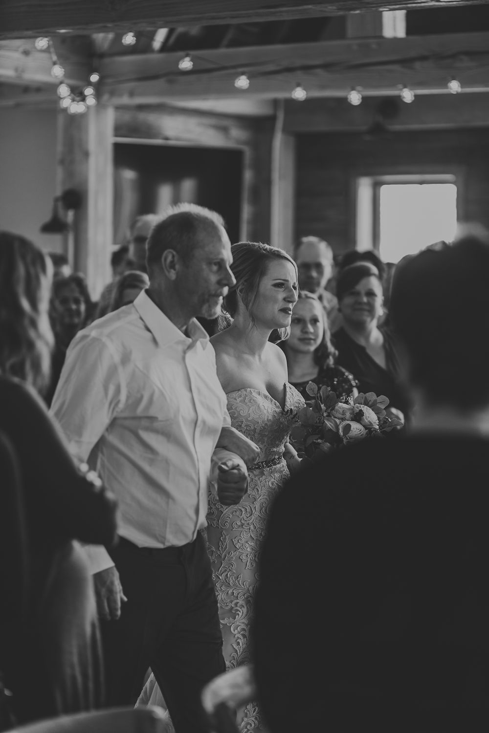 Black and white photo of bride walking down the aisle with her father in a rustic barn ceremony.