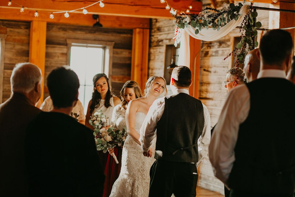 Bride laughs joyfully while holding hands with groom at the altar during a rustic barn wedding.