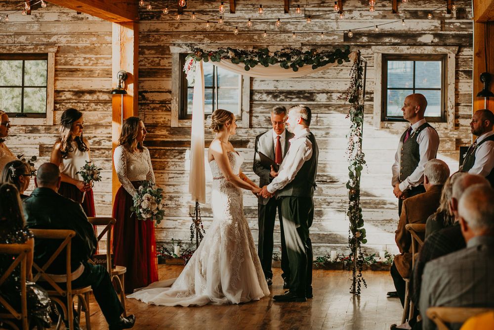 Bride and groom exchange vows at a floral arch altar inside a beautifully lit rustic log cabin venue.