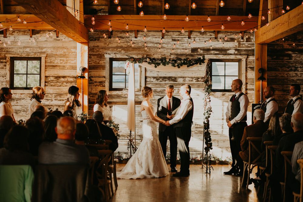 Rustic barn wedding ceremony with bride and groom at the altar, string lights, and wooden walls.