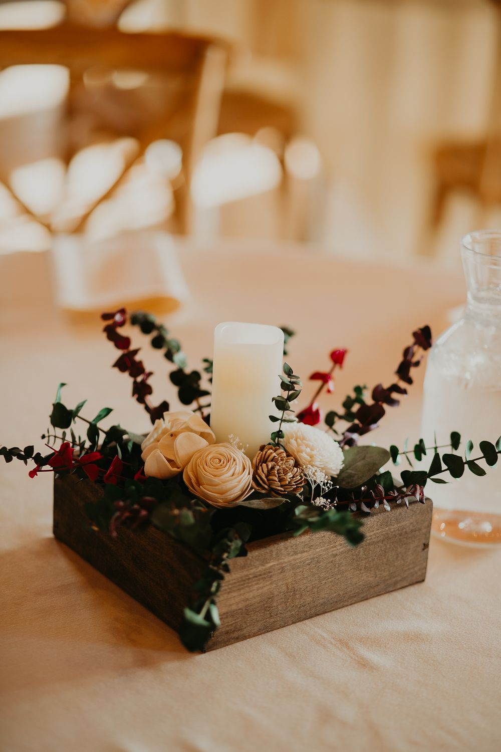 Rustic wooden box centerpiece with white candle, sola flowers, and eucalyptus on reception table.