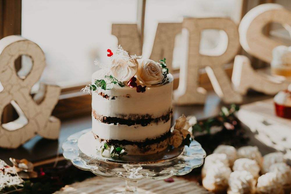 Naked wedding cake topped with roses beside MR and MRS signs at rustic wedding dessert table.