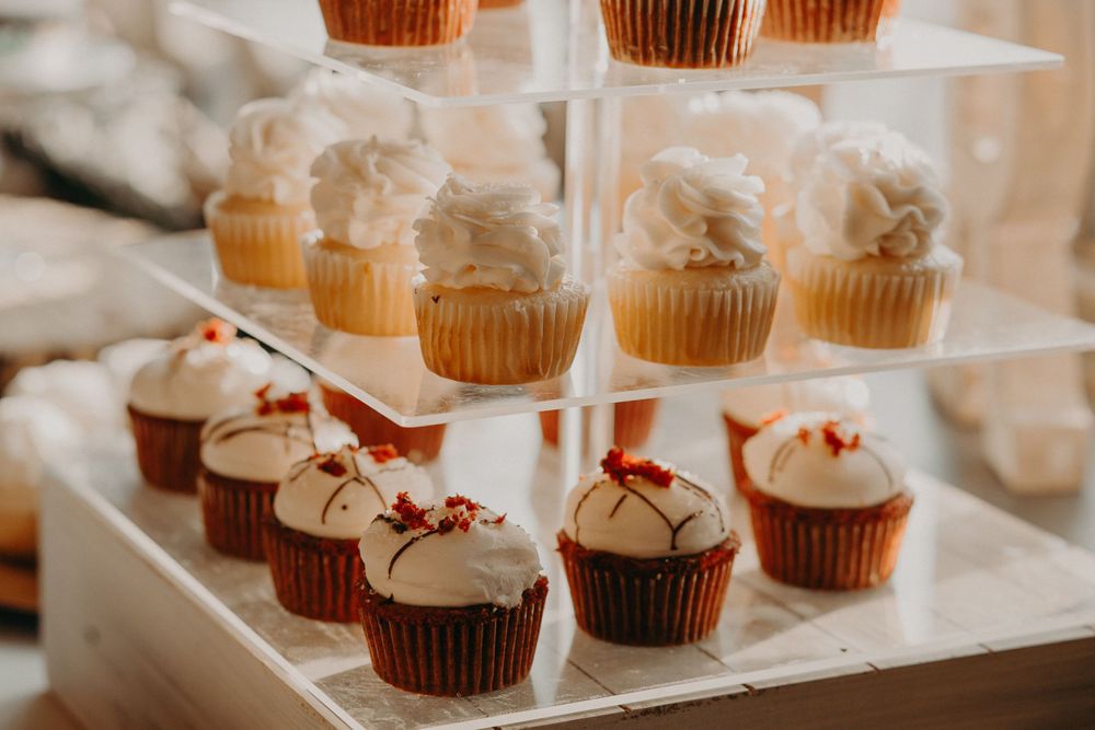 Tiered display of vanilla and red velvet cupcakes with white frosting at wedding dessert table.