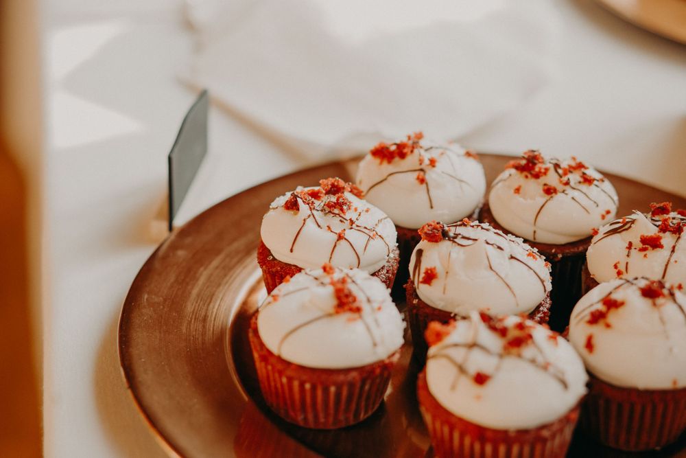 Red velvet cupcakes with white frosting and red sugar decorations on a gold plate at wedding.
