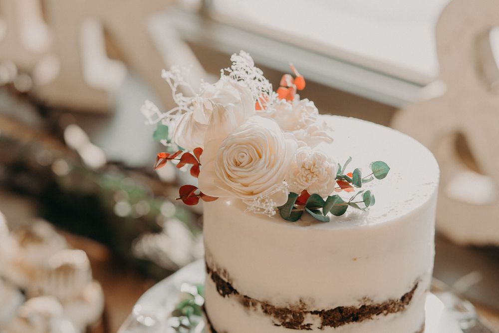 Elegant wedding cake topped with white roses and greenery on a white frosted semi-naked cake.