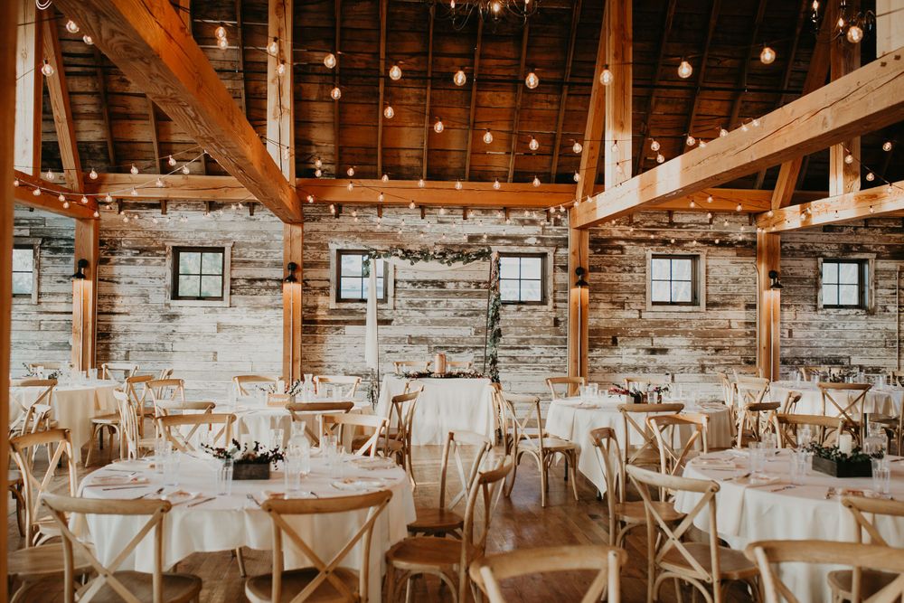 Rustic stone wall barn wedding reception with round tables, white linens, and string lights.