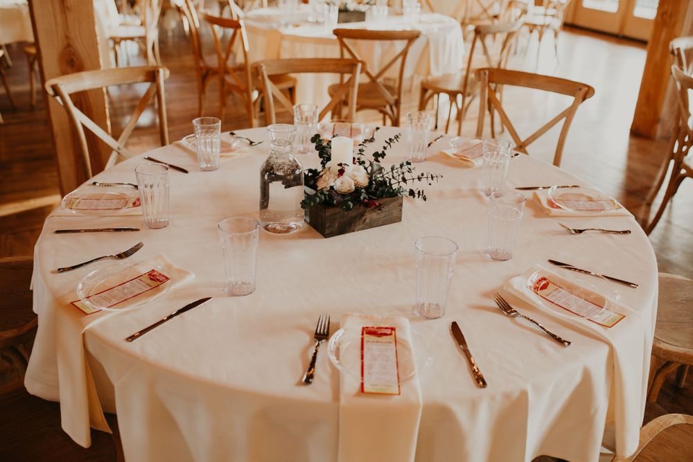 Elegant round wedding reception table with white linen, floral centerpiece, and place settings.