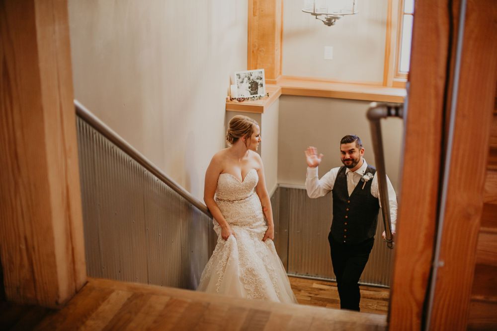 Bride and groom descending wooden staircase at rustic barn wedding venue.