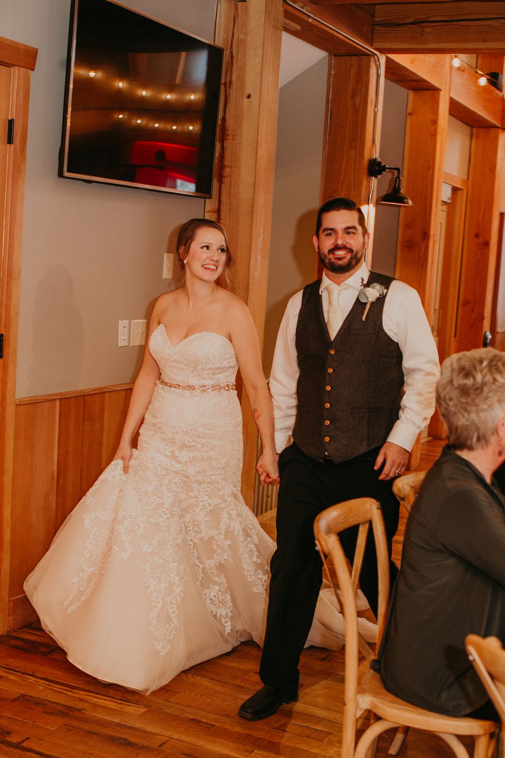 Smiling bride and groom entering rustic barn wedding reception in elegant attire.