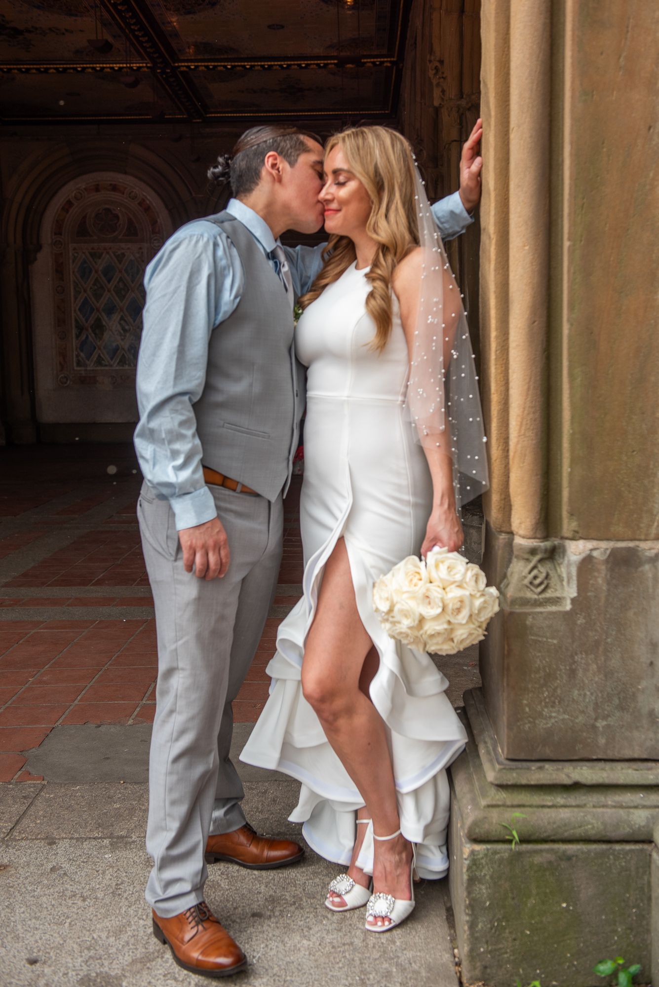 Close-up wedding photo details showing dress, shoes, and bouquet against stone columns.