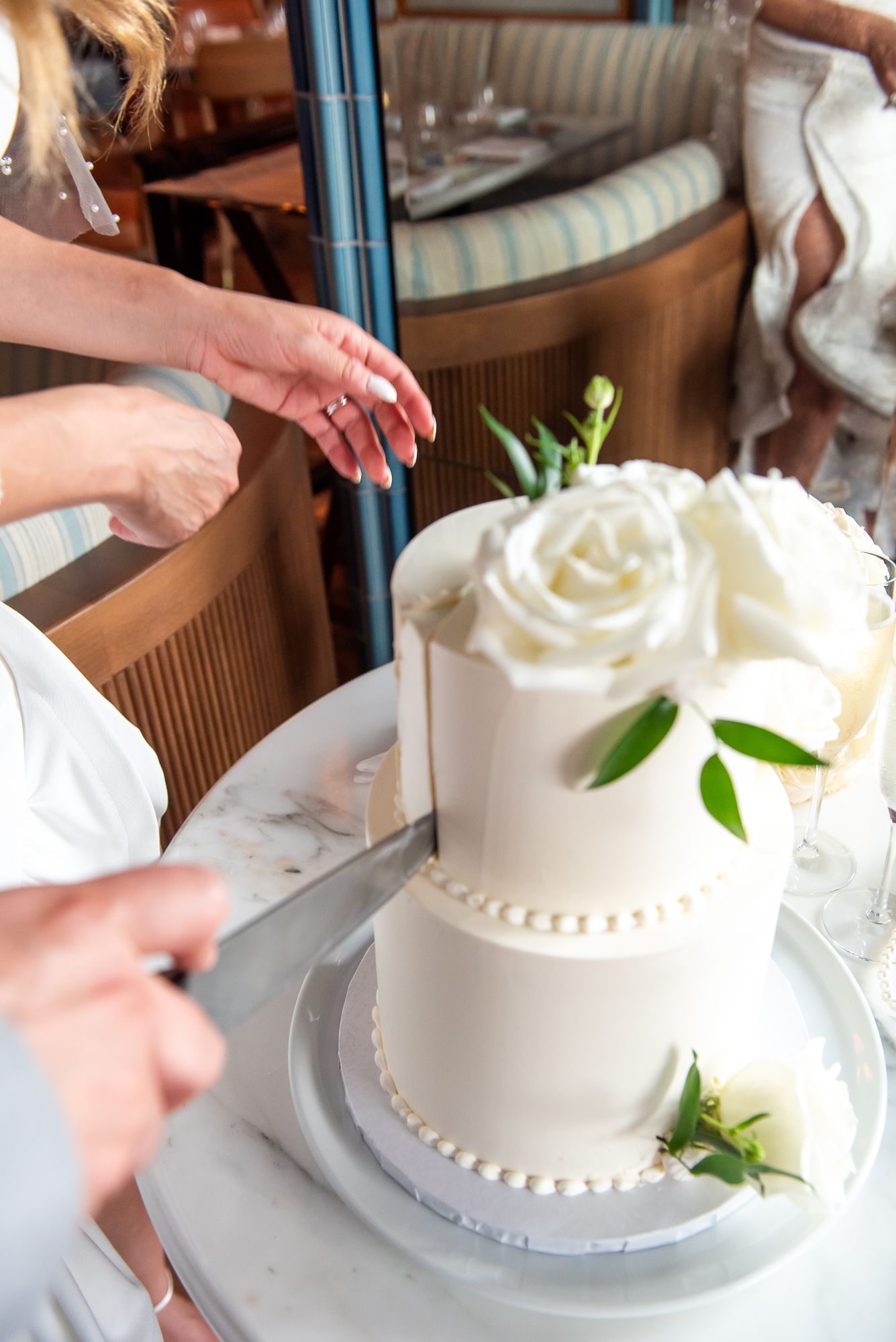 Detailed view of a pristine white wedding cake with pearl beading and fresh rose decorations being cut.