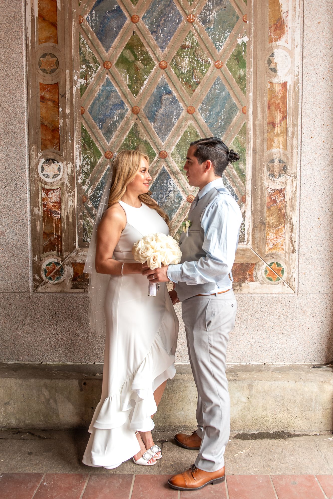 Wedding couple poses against a vintage wall with diamond-patterned frescoes.
