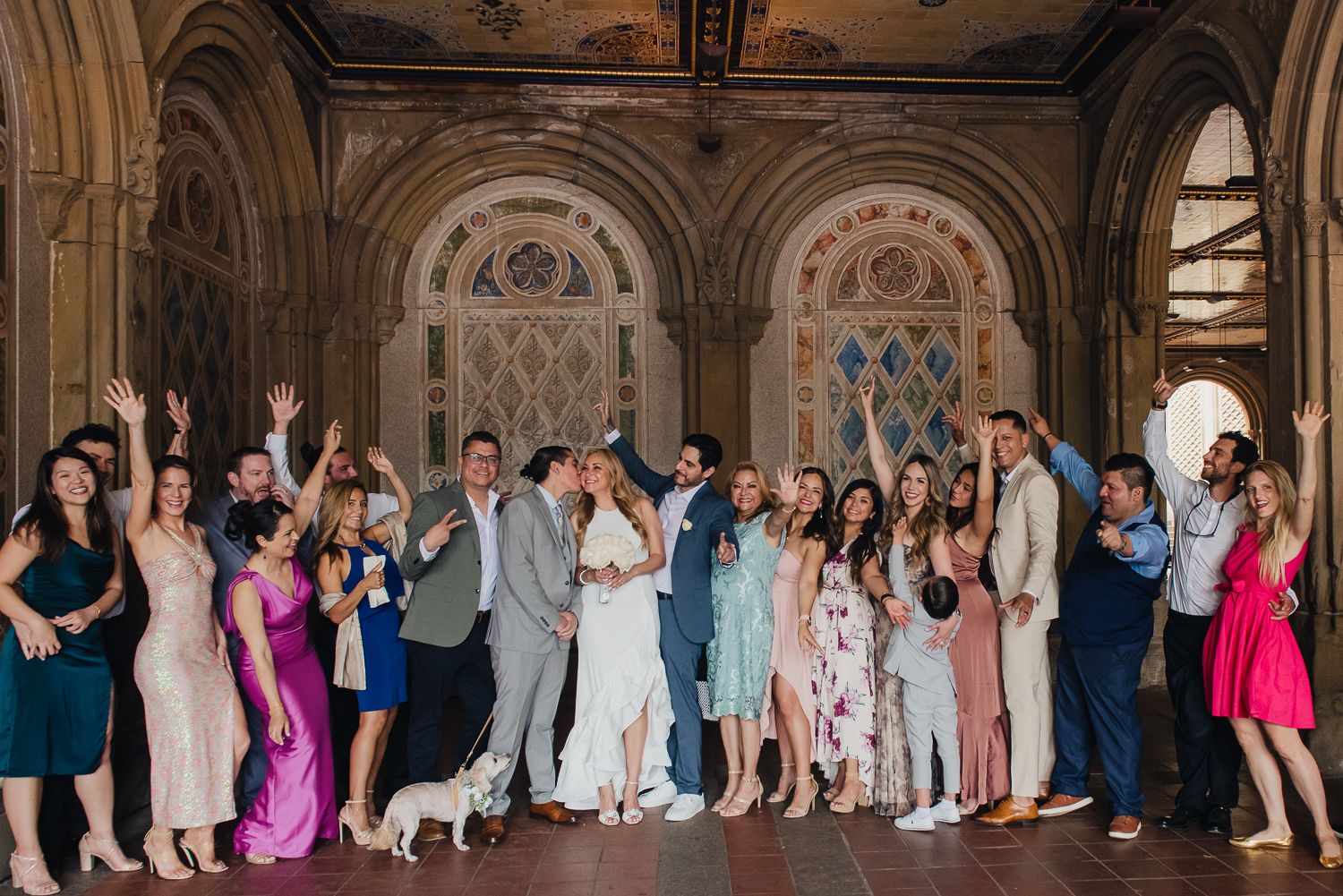Large group wedding photo with guests lined up under elegant arched hallway.
