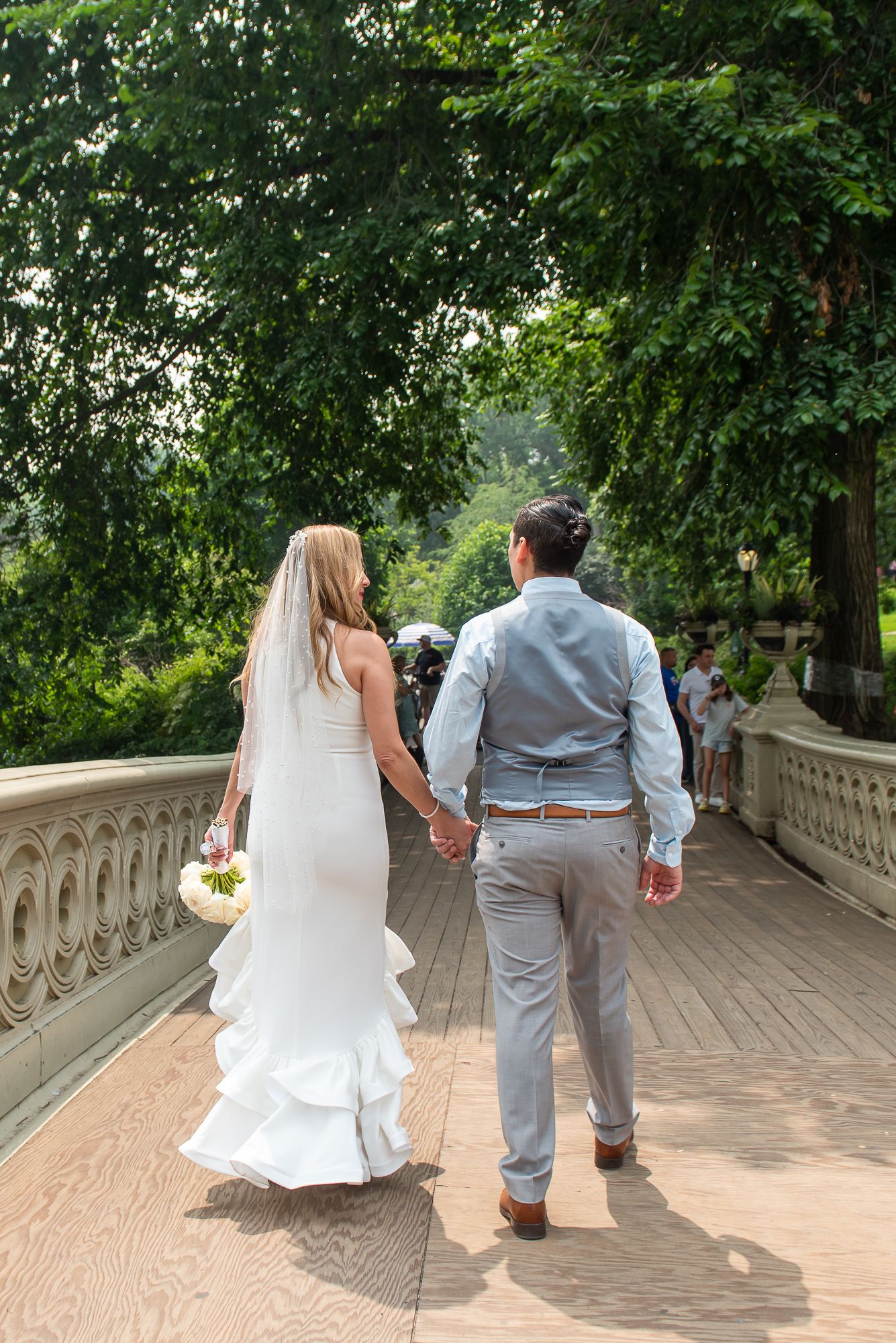Wedding couple walking along the scenic terrace pathway surrounded by green trees.